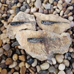 Three black glitter fishing lures on rocks.
