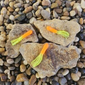 Three colorful fishing flies on rocks surrounded by pebbles.